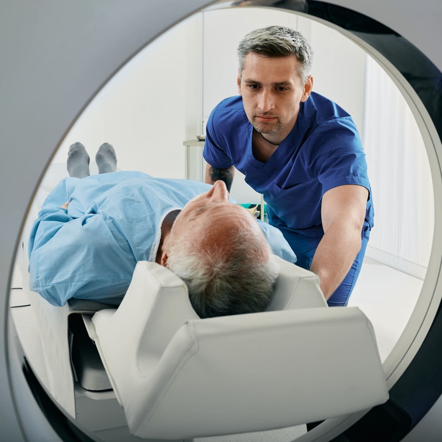 Senior man going into CT scanner. CT scan technologist overlooking patient in Computed Tomography scanner during preparation for procedure